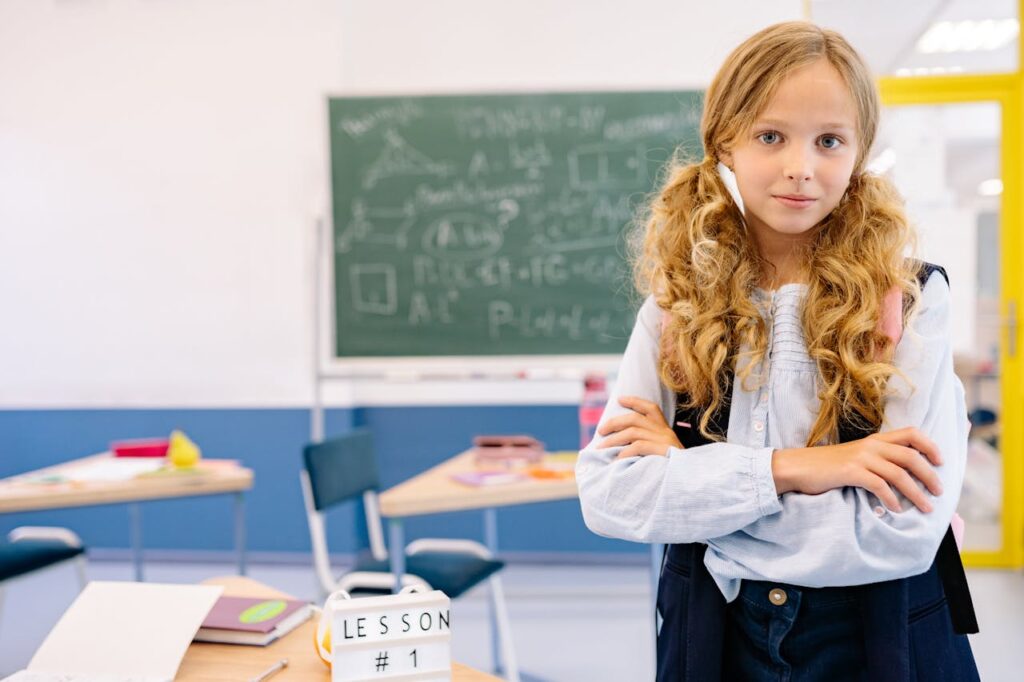 Young girl standing with arms crossed in a classroom setting, embracing confidence and readiness to learn.